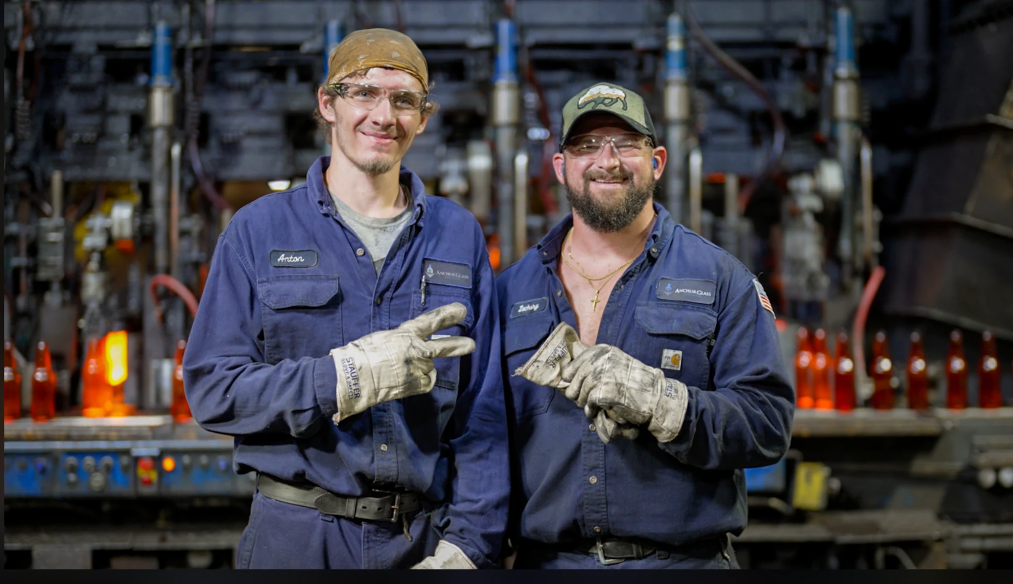 Two Anchor Glass employees standing in front of active production equipment